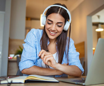 Person wearing headphones smiles while studying with a notebook and laptop.