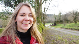 Headshot of Belinda Kirk. In the background is a forest and unpaved swirling countryside road. 