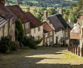 A steep village road with a cobbled roadway, a pretty sceneic village idyll. Countryside stretches into the background beyond the village