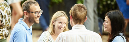 Group of four people standing in a circle chatting and smiling.