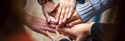 A group of people laying their hands of top of each others hands to indicate a team.