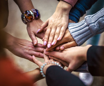 A group of people laying their hands of top of each others hands to indicate a team.