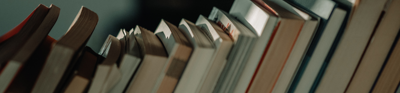 A stack of books are leaned to the right before a blurry grey backdrop.