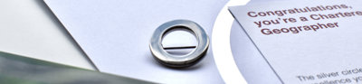 A silver circle lapel pin, a symbol of Chartered Geographer status, next to a card that says 'Congratulations, you're a Chartered Geographer'. 