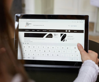 Close-up of a person holding a tablet displaying the website of the RGS-IBG's AREA journal. 