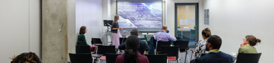 Several people sit in a room facing a presenter.