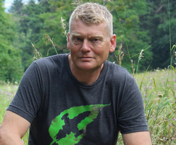 Portrait photograph of Tom Heap in a forest against foreground of flowers and wild grass.