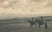 Black and white photograph of two horse riders watching over a large, desolate plain at the foot of the Rockies.