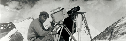 Historic black and white photograph of two explorers taking photographs in a snowy mountainous environment.