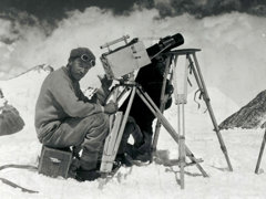 Historic black and white photograph of two explorers taking photographs in a snowy mountainous environment.