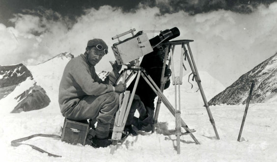 Historic black and white photograph of two explorers taking photographs in a snowy mountainous environment.