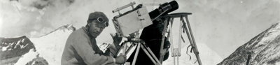 Historic black and white photograph of two explorers taking photographs in a snowy mountainous environment.