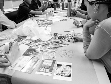 People sitting around a table looking at postcards and drawing