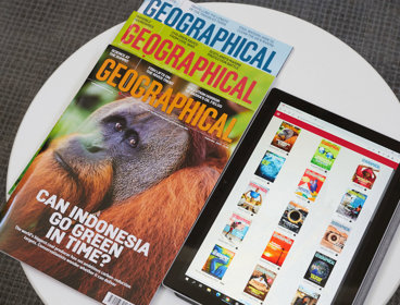 A pile of three print copies of Geographical magazine next to a tablet that displays covers of magazines in the Geographical magazine app.