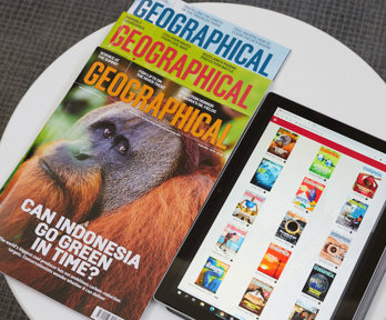 A pile of three print copies of Geographical magazine next to a tablet that displays covers of magazines in the Geographical magazine app.