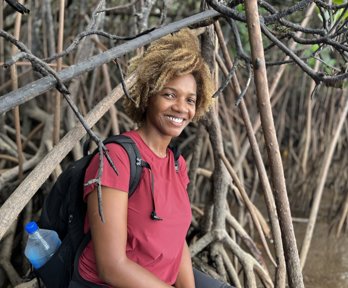 Woman in red t-shirt and wearing a backpack sitting at the edge of mangroves.