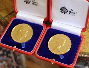 Two gold medals shown in open red boxes with blue velvet, the words 'The Royal Mint' are written on each box