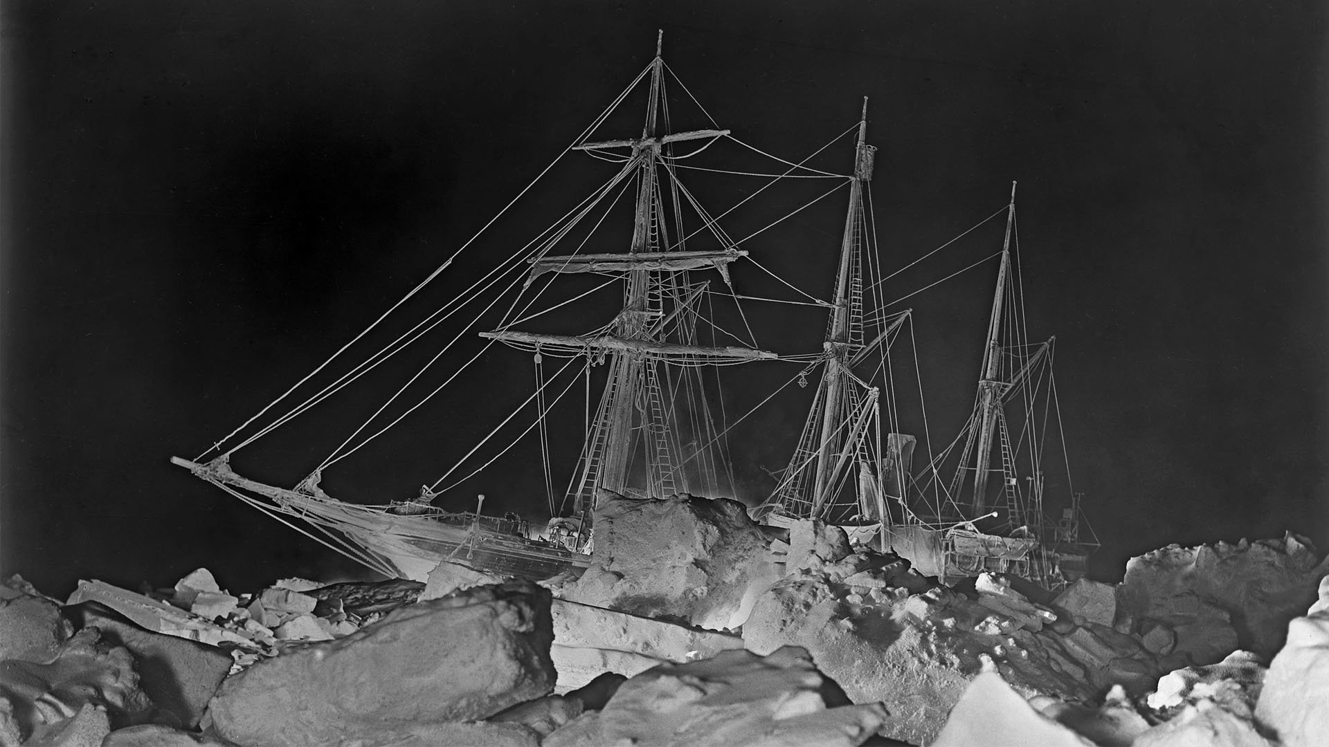 Old black and white photo of the Endurance stuck in ice at night.