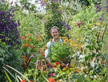 Monty Don standing surrounded by plants and flowers in an abundant garden.