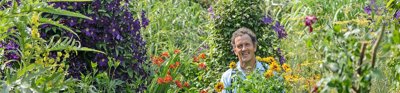 Monty Don standing surrounded by plants and flowers in an abundant garden.