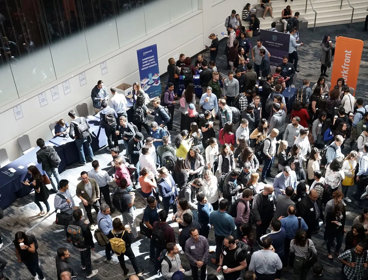 Conference hall with people chatting and gathering around stalls.