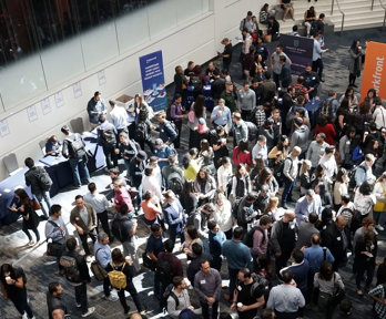 Conference hall with people chatting and gathering around stalls.