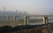 A bridge over a near-dry river with in the background a city and a smoggy sky.