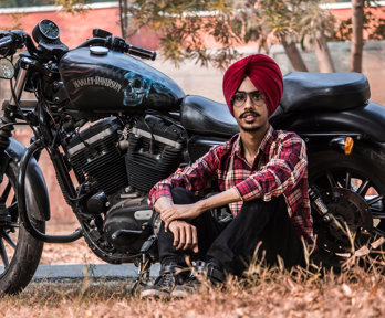 A man in a red turban sitting up against a Harley Davidson motorbike