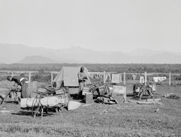 Four people camping in a vast field, in Fort Hertz, North Burma. Mountains can be seen far in the background. This visual is not in colour. 