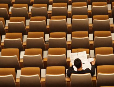 Person sits alone in a lecture hall whist reading through several papers.