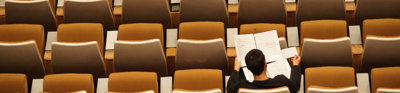 Person sits alone in a lecture hall whist reading through several papers.