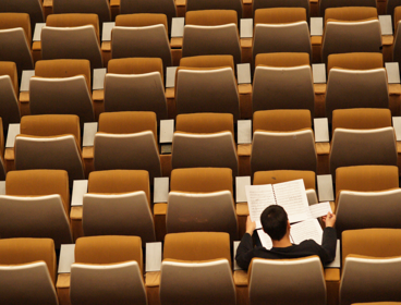 Person sits alone in a lecture hall whist reading through several papers.