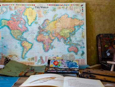 Map of the world poster with a book, paints and easel on the table in front.