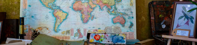 Map of the world poster with a book, paints and easel on the table in front.