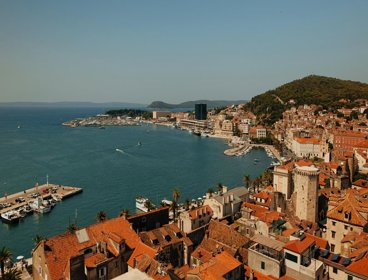 A view over a Mediterranean town by the sea. The roofs are orange tile and several jettys for boats can be seen