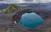 A blue, geothermal spring in a rugged, desolate mountainous landscape.