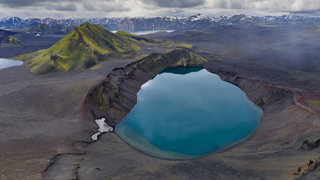 A blue, geothermal spring in a rugged, desolate mountainous landscape.