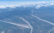 Aerial view of a braided river winding through fields and scattered towns under a partly cloudy sky.