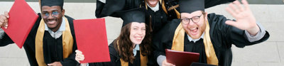 Group of five people in graduation gowns celebrating and raising their certificates.