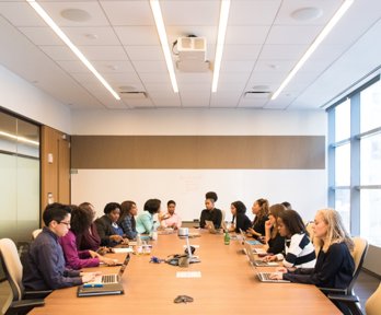 People sat around a long desk typing on laptops in a meeting