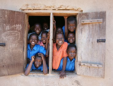 A selection of African children looking out of a classroom window and smiling. 