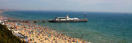 A view over a beach packed with people with a pier jutting out into the sea