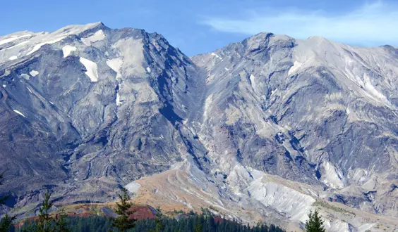 Mount St Helens with blue sky and trees in the foreground.