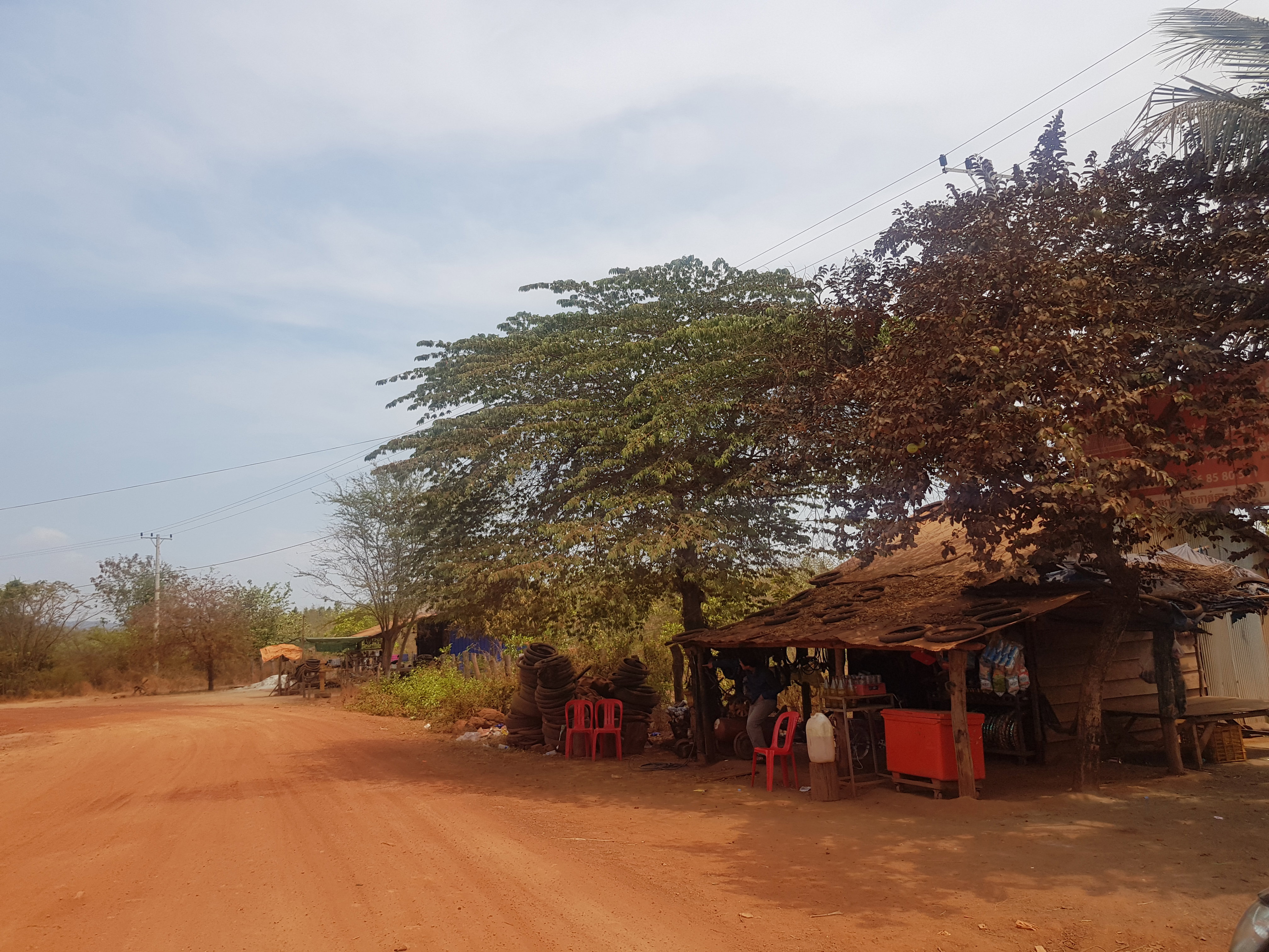 Two market shops amongst trees on the side of a dirt road. 