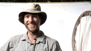 Headshot of Jan Mertens. He is wearing a safari style outfit and hat and is smiling happily.