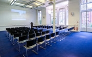 Lecture theatre style chairs facing a projector at the front in a brightly lit room.