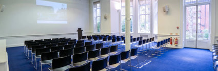 Lecture theatre style chairs facing a projector at the front in a brightly lit room.