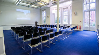 Lecture theatre style chairs facing a projector at the front in a brightly lit room.