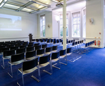 Lecture theatre style chairs facing a projector at the front in a brightly lit room.