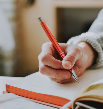 Person holding a pen and writing in an open notebook on a table.